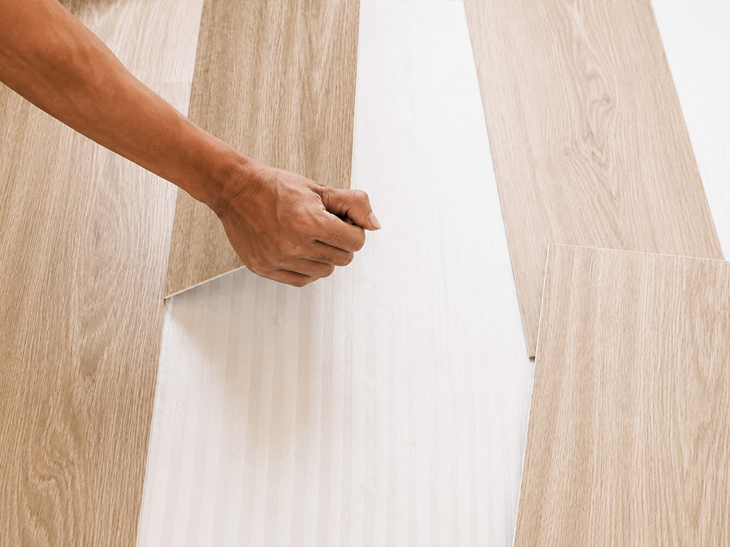 Installer fitting a light oak-look vinyl plank into place